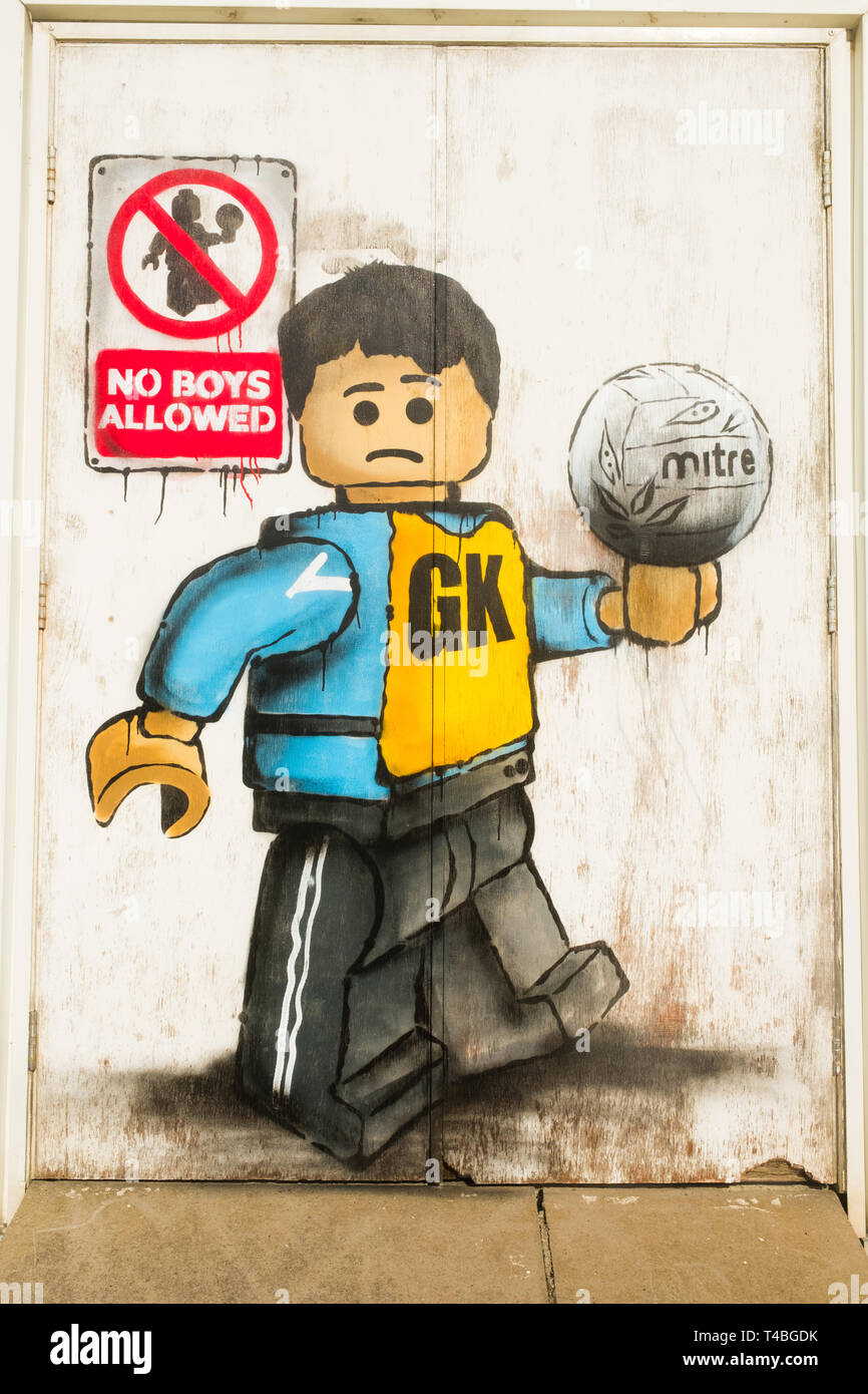 'No Boys Allowed' Graffiti by James Ame - Ame72 (The `Lego Guy)  -  on the exterior of the leisure centre in Aberystwyth, showing an unhappy boy in a GK  netball vest, in reference to the ban by the Urdd ( a welsh langiage youth organisation) on boys competing in netball competitions.  March 10 2019 Stock Photo